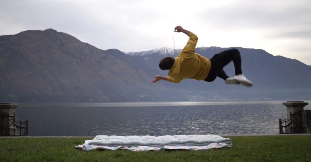 A person flipping sideways by a mountainous lakeside