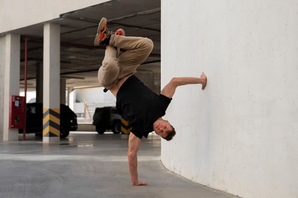 An individual does a handstand against a white wall in a parking garage