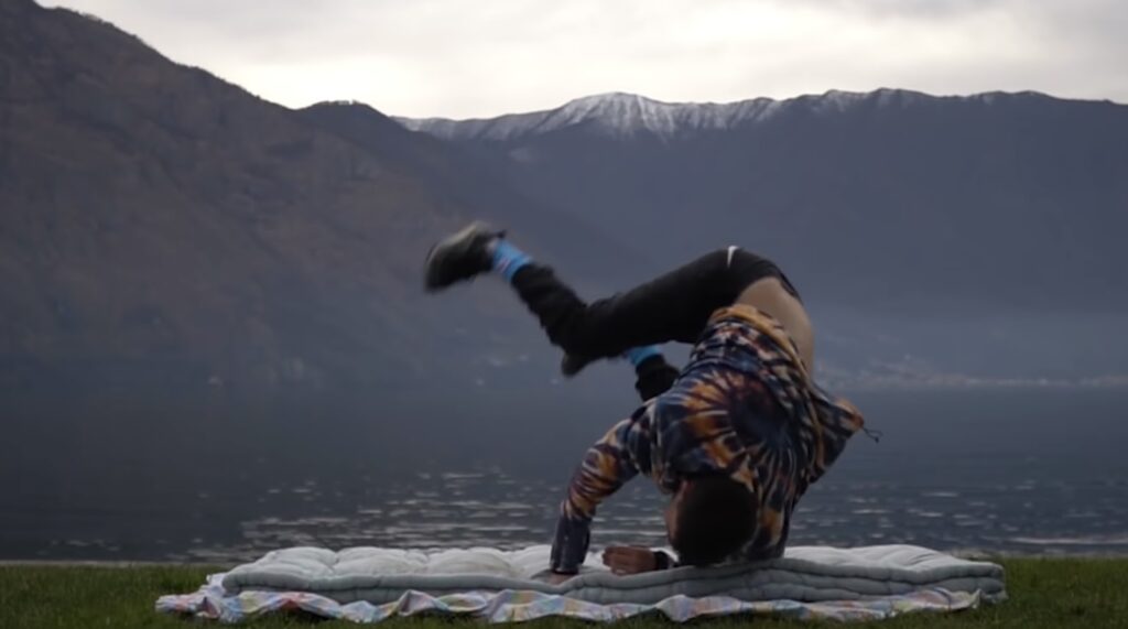 A person breakdancing near a lake with mountains