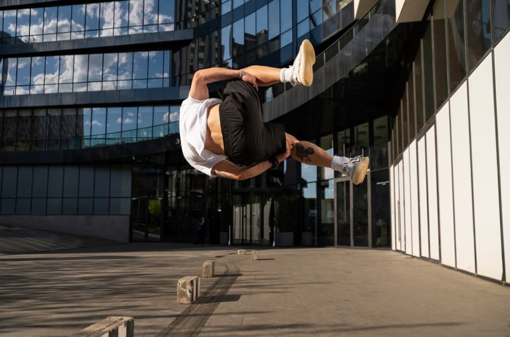 A person backflipping in an urban plaza with mirrored buildings