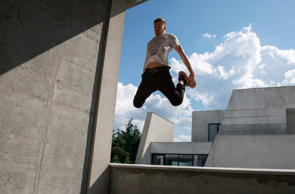 A man jumps between buildings against a clear sky