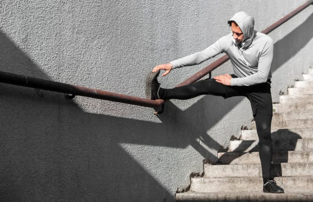 Man warming up his legs using a railing and standing on the stairs