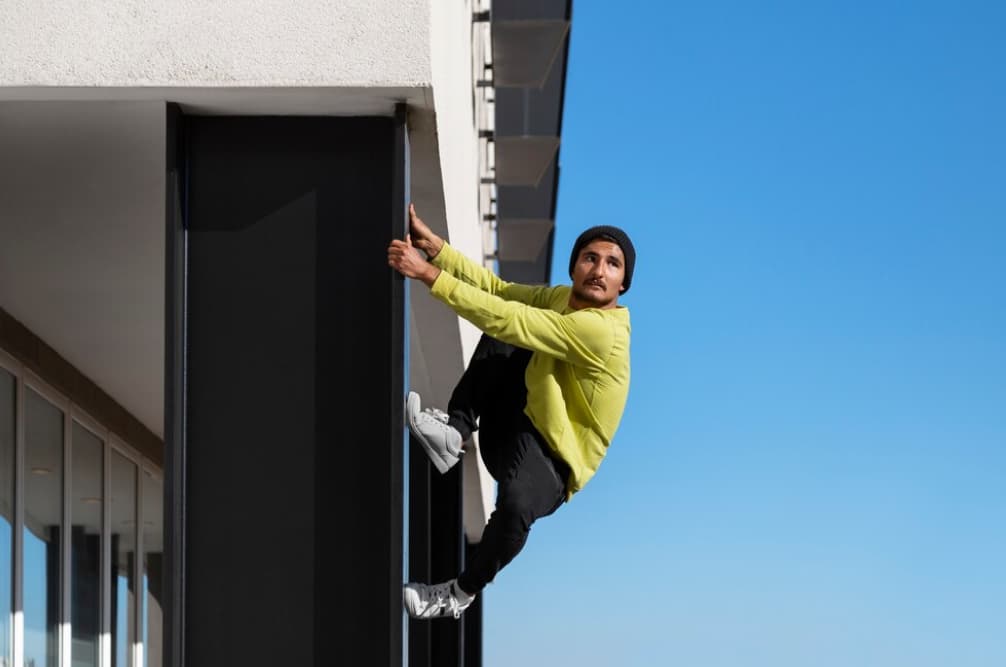 A man in a yellow shirt climbs up the side of a modern building