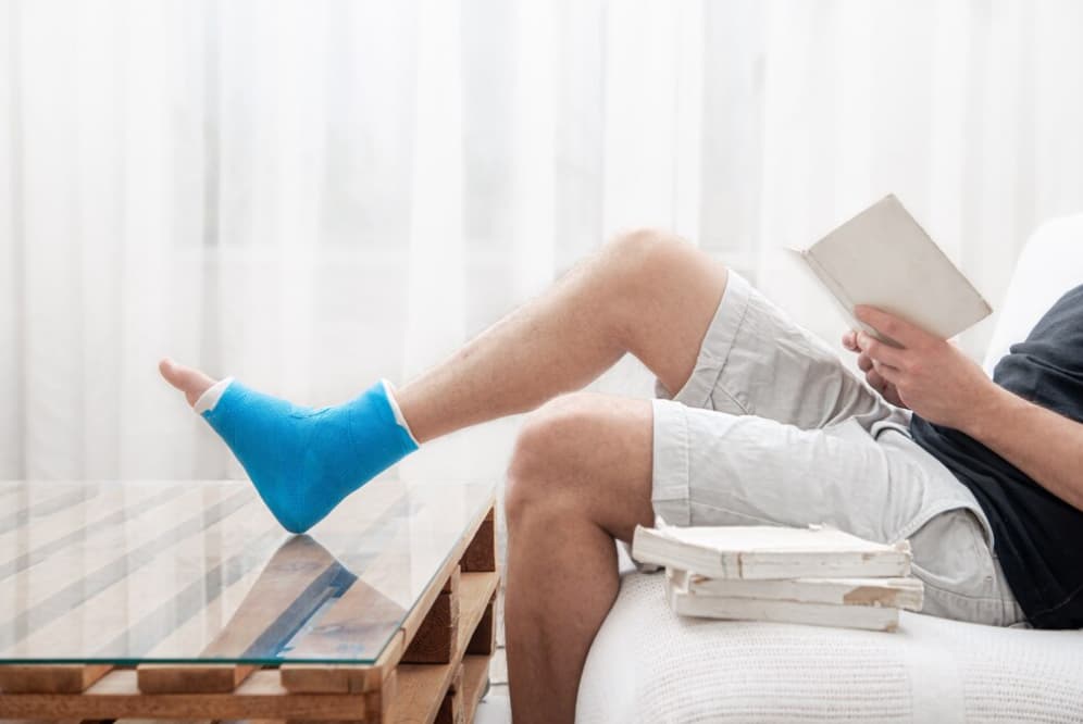 An individual with a blue cast on their leg reading a book