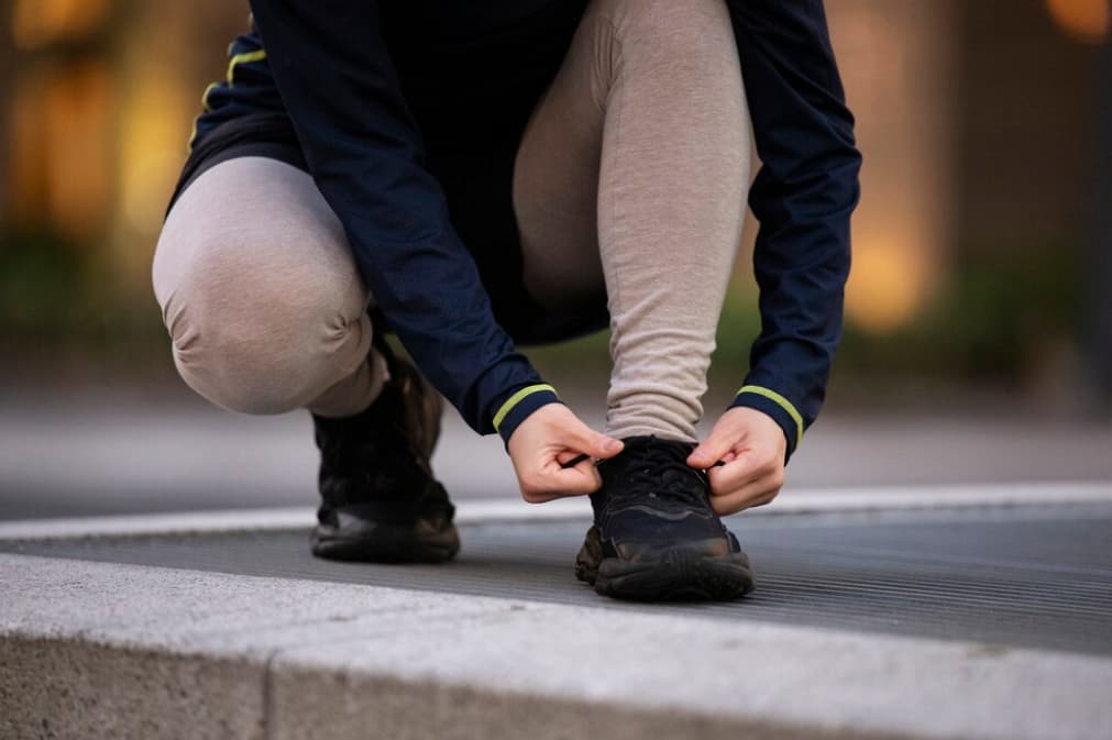 A runner tying their shoe on a city sidewalk