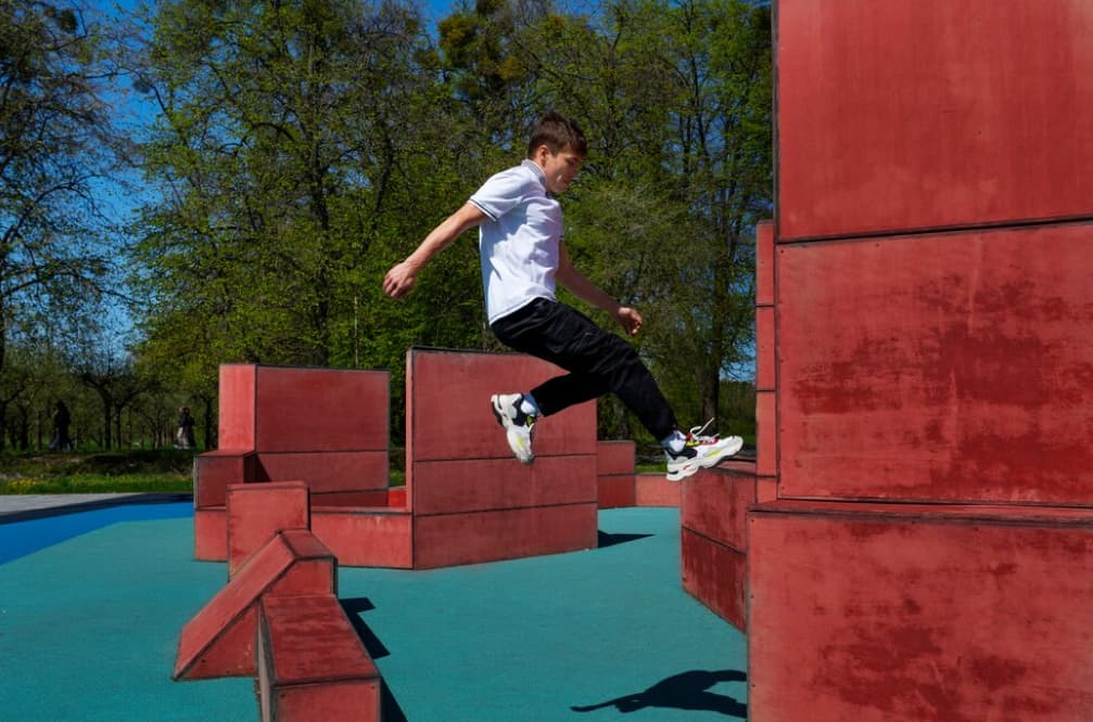 A person in a white shirt jumps over red blocks in a park