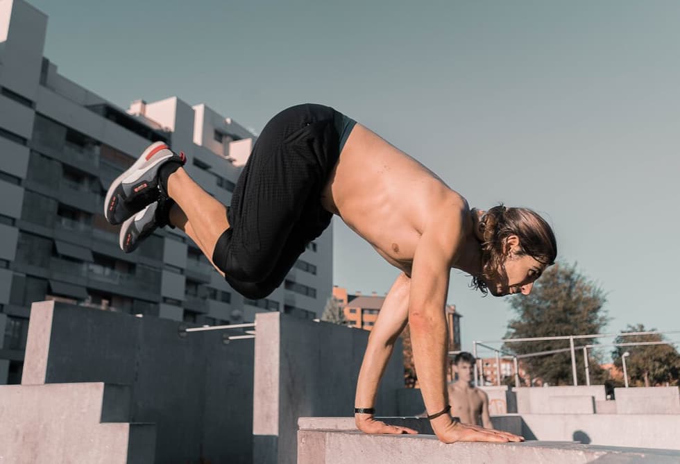 A person balances on hands in a planche position at a parkour park