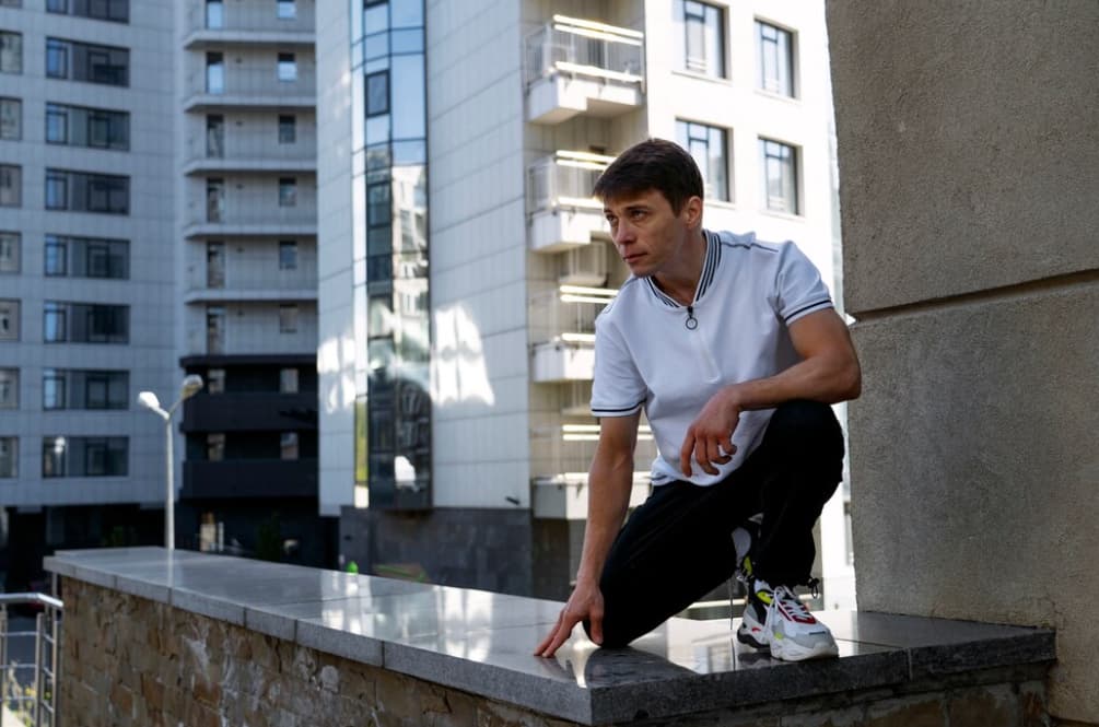 A man crouches thoughtfully atop a high wall in the city