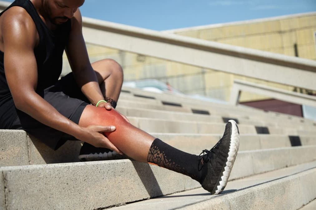A man sitting on stairs, holding his shin in pain