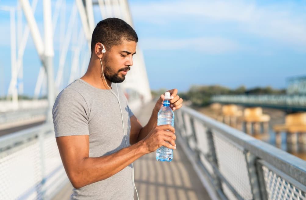 man in gar t-shirt opening bottle of water and standing on the bridge